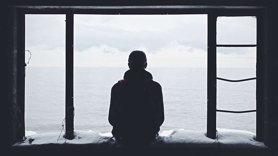 Einsamer nachdenklicher Junge im Schnee sitzend bei Kälte und nach draußen zum Meer schauend Traurig Allein